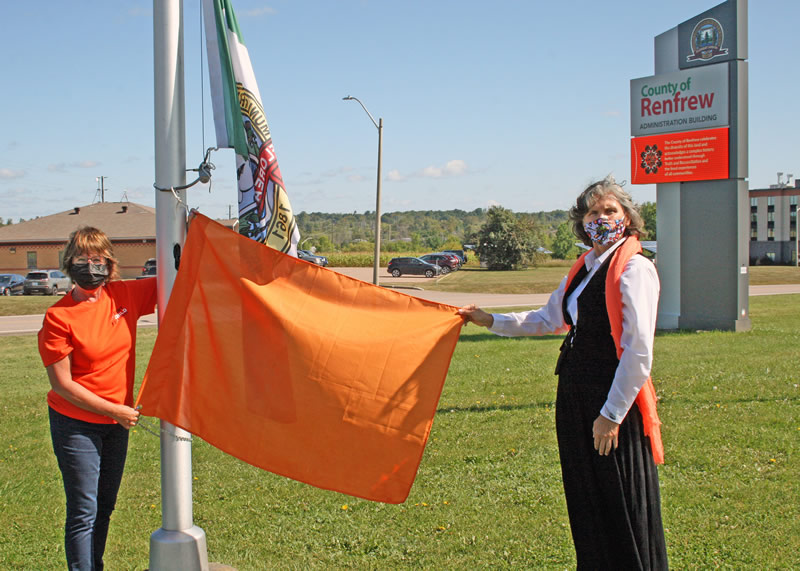 Warden Debbie Robinson and Chief Wendy Jocko raise an orange flag outside the County of Renfrew Administration building